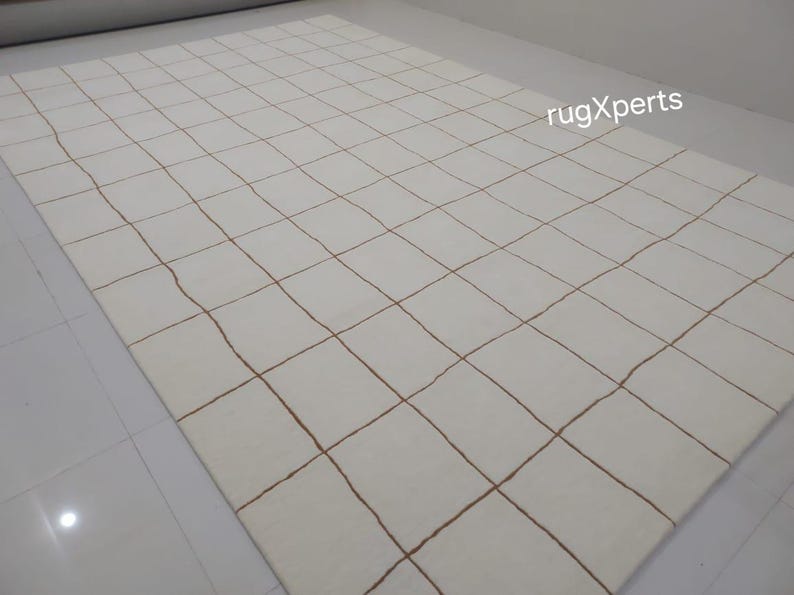 May include: White rug with a grid pattern of thin brown lines. The rug is made of a soft, woven material.