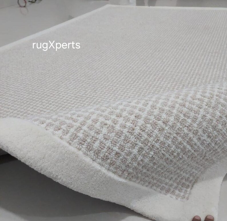 May include: A white and cream colored rug with a diamond pattern. The rug has a thick, fluffy texture and a white border.