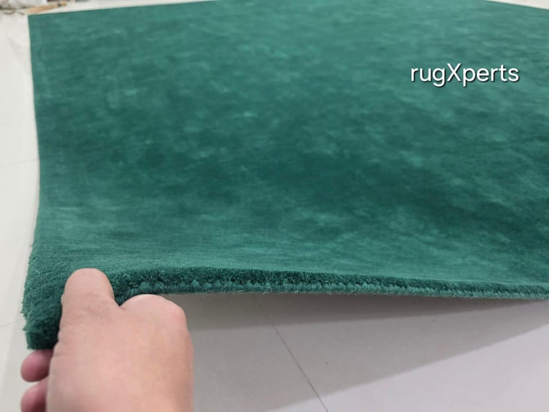 May include: A close-up of a green rug with a textured surface. The rug is a solid colour and appears to be made of a soft material. The text "rugXperts" is visible in the upper right corner.