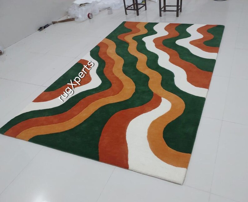 May include: A rectangular rug with a wavy pattern in green, white, orange, and rust colors. The rug has a soft texture and is suitable for living rooms or bedrooms. The text "rugXperts" is visible on the rug.