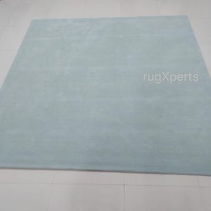 May include: A large, rectangular, light blue rug with a soft, plush texture. The rug is displayed on a white tiled floor. The text "rugXperts" is visible on the rug.