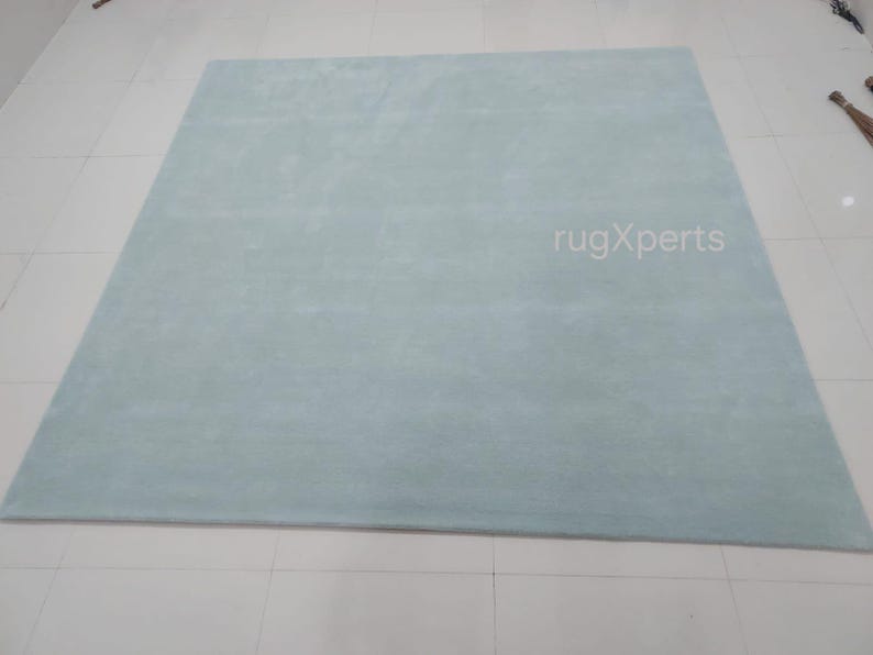 May include: A large, rectangular, light blue rug with a soft, plush texture. The rug is displayed on a white tiled floor. The text "rugXperts" is visible on the rug.