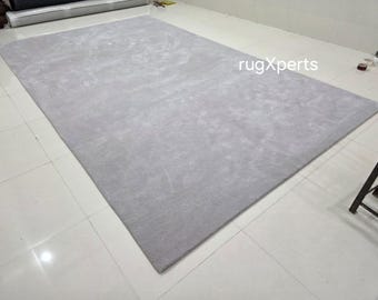 Puede incluir: Una alfombra grande, rectangular, de color gris claro. La alfombra tiene una textura suave y afelpada y está colocada sobre un suelo de baldosas blancas. La alfombra es de color liso y parece estar hecha de un material tejido. La alfombra es de color neutro y complementaría muchos estilos de diseño de interiores.