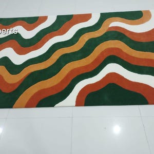 May include: A rectangular rug with a wavy pattern in shades of green, orange, white, and rust. The rug's design features flowing, organic lines that create a visually appealing and modern aesthetic. The rug is suitable for living rooms and bedrooms.