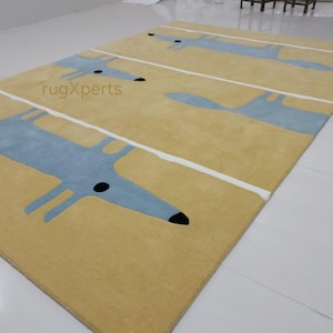 May include: A yellow rug with a repeating pattern of blue fox silhouettes. The rug has white stripes running horizontally across the surface. The text "rugXperts" is visible in the center of the rug.