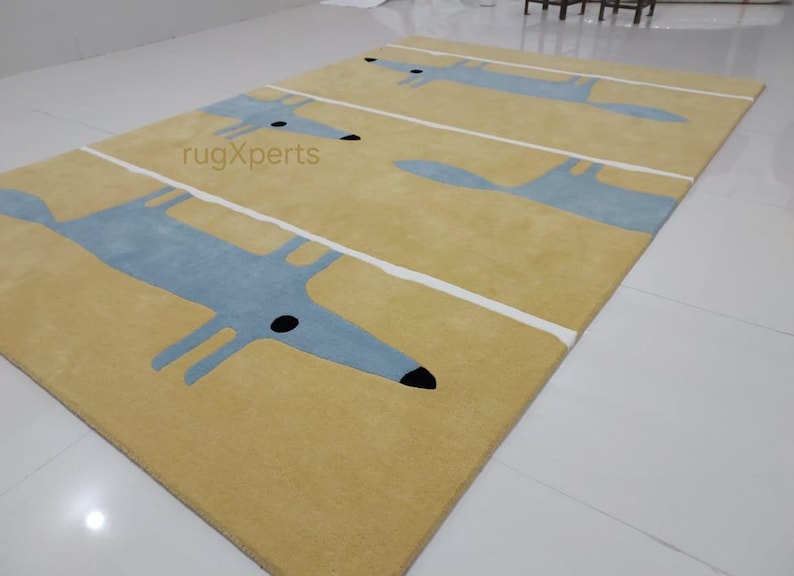 May include: A yellow rug with a repeating pattern of blue fox silhouettes. The rug has white stripes running horizontally across the surface. The text "rugXperts" is visible in the center of the rug.