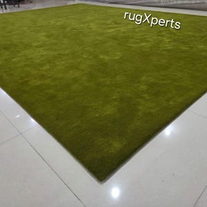 May include: A large, rectangular, green rug with a plush texture. The rug is a solid colour and covers a large area of the floor. The text "rugXperts" is visible in the upper right corner.