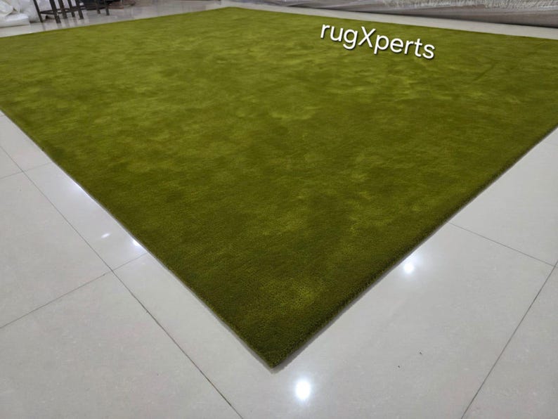 May include: A large, rectangular, green rug with a plush texture. The rug is a solid colour and covers a large area of the floor. The text "rugXperts" is visible in the upper right corner.