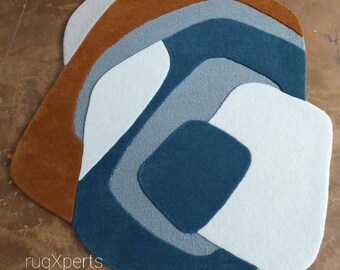 Puede incluir: Alfombra de área abstracta con un diseño moderno que presenta una combinación de colores azules, grises, blancos y marrones. La alfombra tiene una forma única y orgánica y un aspecto texturizado en capas.