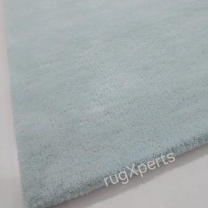 May include: A rectangular, light blue rug with a soft, textured surface. The rug has a plush appearance and is likely made of a comfortable material. The rug's color is a muted, pastel shade of blue.