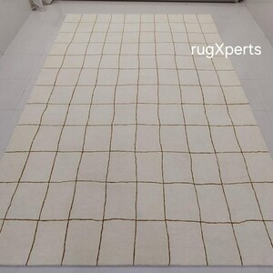 May include: A white rug with a grid pattern of brown lines. The rug is made of wool and has a soft, luxurious feel.