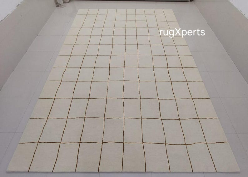 May include: A white rug with a grid pattern of brown lines. The rug is made of wool and has a soft, luxurious feel.