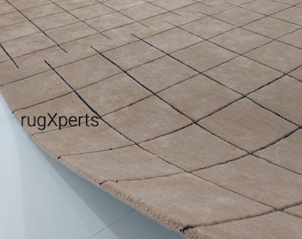 May include: A beige rug with a geometric pattern of black lines forming squares. The rug is rolled up and the edge is visible.