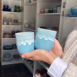 Op de afbeelding: Een witte keramische mok met een zwarte handgreep en de tekst "But first, coffee" in een zwarte, handgeschreven lettertype. De mok staat op een wit oppervlak.