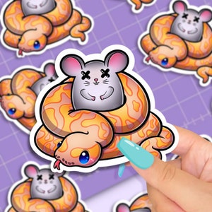 May include: A sticker featuring a cartoon illustration of a snake with a mouse on its head. The snake is orange and yellow with black eyes. The mouse is gray with black eyes and a black X over its eyes. The sticker is on a purple background.