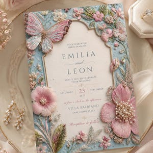 Premium high-quality editable butterfly wedding invitation featuring embroidered blush pink florals, delicate botanical details, pearl accents, and a soft powder blue background with an elegant gold arch frame. Luxury Canva template perfect for romantic, garden, spring, and elegant weddings.