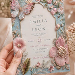 Premium high-quality editable butterfly wedding invitation featuring embroidered blush pink florals, delicate botanical details, pearl accents, and a soft powder blue background with an elegant gold arch frame. Luxury Canva template perfect for romantic, garden, spring, and elegant weddings.