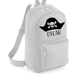 Może przedstawiać: Szary plecak z płótna z czarnym kapeluszem pirata i wzorem czaszki i skrzyżowanych kości. Nazwa "OSCAR" jest nadrukowana pod wzorem.