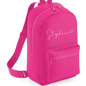Könnte beinhalten: Ein leuchtend rosa Rucksack mit einem weißen Reißverschluss und einem weißen gestickten Namen "Stephanie" mit einem Herz.