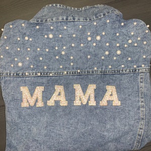 May include: A blue denim jacket with white pearl embellishments and the word "MAMA" spelled out in gold sequins.