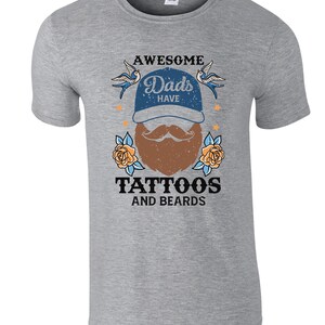 May include: Grey t-shirt with a graphic design that says "Awesome Dads Have Tattoos and Beards". The graphic features a cartoon beard with a moustache, a baseball cap, and two birds.