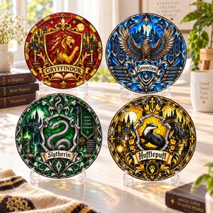 May include: Four circular decorative plates featuring stained glass style artwork of the four house crests: Gryffindor with a lion, Ravenclaw with an eagle, Slytherin with a snake, and Hufflepuff with a badger, each displayed on clear stands.