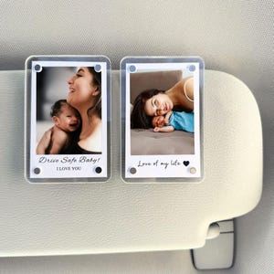 以下が含まれることがあります： 母親と赤ちゃんの写真が入った、2つの透明なアクリルフォトホルダー。1つには「Drive Safe Baby! I LOVE YOU」と書かれています。もう1つは、ハートマーク付きで「Love of my life」と書かれています。サンバイザーに取り付けられています。