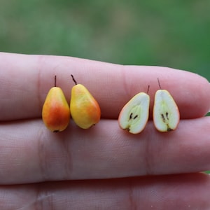 Puede incluir: Cuatro peras en miniatura, dos enteras y dos cortadas por la mitad, con piel amarilla y naranja y pulpa blanca. Las peras se muestran en una mano.