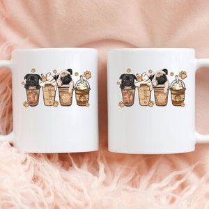 May include: Two white ceramic mugs with a design of four pugs in coffee cups. The pugs are wearing different expressions and are holding different types of coffee drinks.