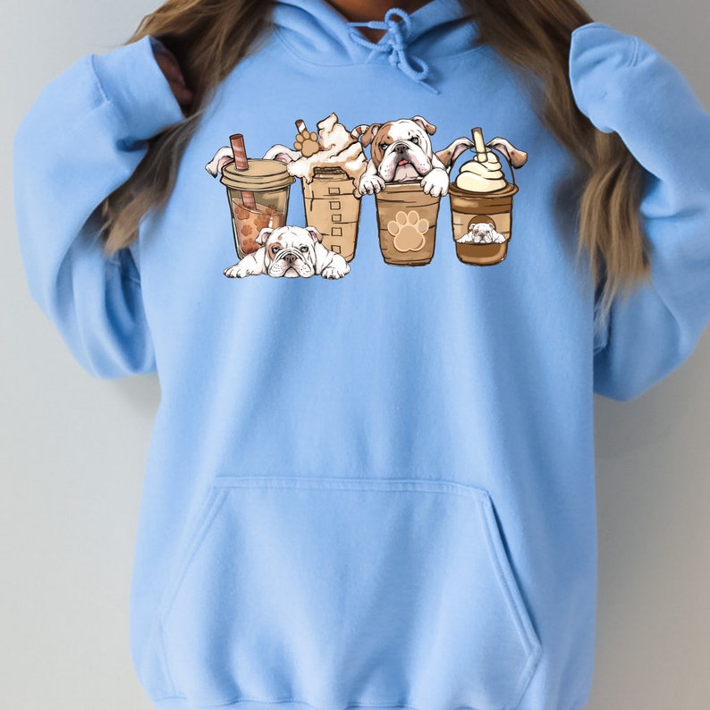 May include: A light blue hoodie with a graphic of four bulldogs peeking out of coffee cups. The bulldogs are brown and white with black noses. The coffee cups are brown with white lids and have a paw print design.