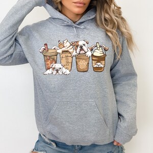 May include: Gray hooded sweatshirt with a graphic of four bulldogs peeking out of coffee cups. The bulldogs are white with brown spots and the coffee cups are brown with white lids.