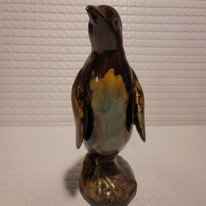 Könnte beinhalten: Eine Keramik-Pinguin-Figur mit brauner, grüner und gelber Glasur. Der Pinguin steht aufrecht mit dem Kopf nach oben geneigt.