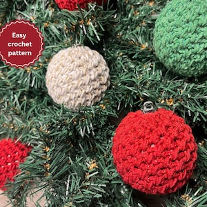 以下が含まれることがあります： 赤、緑、白、金で編まれたクリスマスオーナメントで飾られたクリスマスツリーのクローズアップ。オーナメントはシンプルなステッチパターンで作られており、質感があります。画像には「簡単な編み物パターン」というテキストが表示されています。