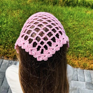 May include: A light pink crochet headscarf featuring an openwork diamond pattern with a scalloped edge. The triangular accessory is crafted from yarn and displays a repeating lattice design that covers the top portion of the head.