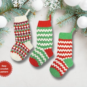 Puede incluir: Tres calcetines de Navidad hechos a mano con ganchillo en rojo, verde y blanco. Los calcetines tienen varios patrones y colores, con un puño y una presilla blancos para colgar. La imagen también incluye el texto "Easy crochet pattern".