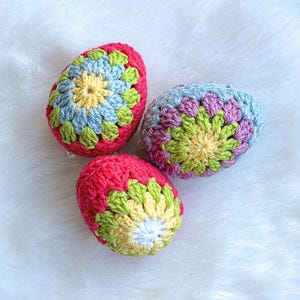 Three crocheted Easter eggs in a variety of colors, including pink, blue, green, and yellow. The eggs are decorated with a flower pattern.