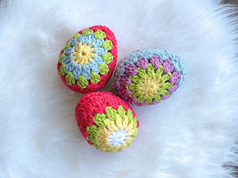 Three crocheted Easter eggs in a variety of colors, including pink, blue, green, and yellow. The eggs are decorated with a flower pattern.