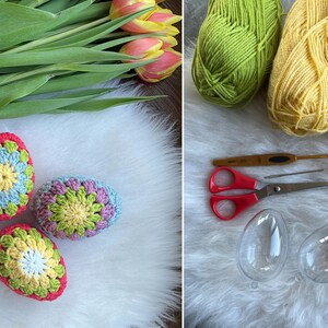 Three crocheted Easter eggs in blue, green, and pink with a yellow center. The eggs are sitting on a white fluffy surface. There are also two clear plastic Easter eggs, scissors, yarn, and a crochet hook on a white fluffy surface.