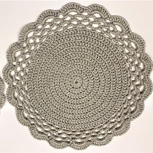 May include: Two gray crocheted placemats. The placemats are round with a scalloped edge. The center of the placemats have a spiral design. The placemats are made of a soft, textured yarn.