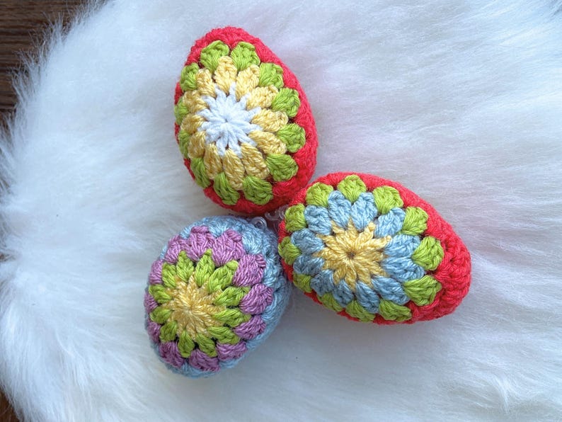 Three crocheted Easter eggs in different colors and patterns. The eggs are red, blue, and pink with yellow and green accents.
