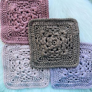 Könnte beinhalten: Vier quadratische Häkeluntersetzer mit einem zentralen Blumenmotiv und komplexen Stichen. Das Set enthält ein altrosa, ein dunkelbraunes, ein helllavendelfarbenes und ein blassfliederfarbenes Quadrat mit jeweils detailliertem Muster.