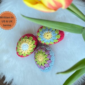Three crocheted Easter eggs in a variety of colors, including pink, green, blue, yellow, and white. The eggs are sitting on a white fluffy surface.