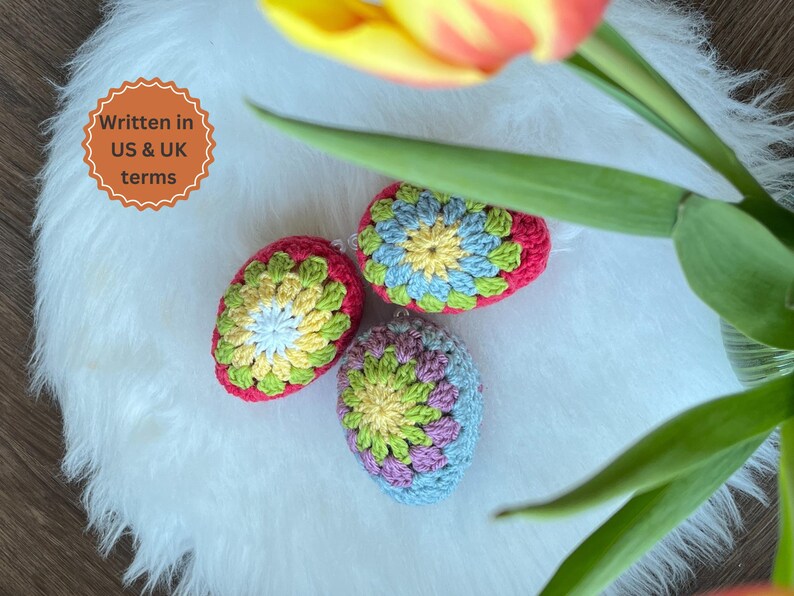Three crocheted Easter eggs in a variety of colors, including pink, green, blue, yellow, and white. The eggs are sitting on a white fluffy surface.