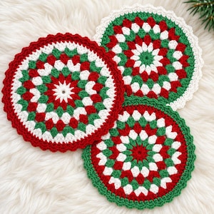 May include: Three circular crochet coasters featuring a radial pattern in red, white, and green yarn. Each coaster has a scalloped edge and a dense, textured stitch design, arranged in a cluster to display the colorful, repeating geometric motifs.