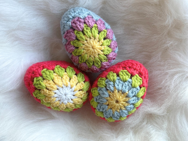 Three crocheted Easter eggs in a variety of colors, including pink, blue, yellow, and green. The eggs are decorated with a flower pattern.