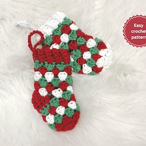 May include: A handmade crochet Christmas stocking in red, green, and white. The stocking features a classic granny square pattern and a red cuff and hanging loop. The image includes the text "Easy crochet pattern".