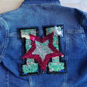 May include: A blue denim jacket with a large sequined star patch on the back. The star is red, silver, and green.
