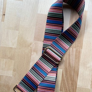 May include: A striped fabric bag strap with gold hardware and two metal clasps. The strap is brown, pink, green, blue, and black.
