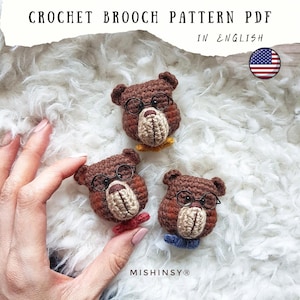 May include: Crochet brooch pattern PDF in English. The image shows three handmade brown bear brooches with glasses and bow ties in yellow, red, and blue. The brooches are on a white, fluffy surface. The brand name Mishinsy is visible.