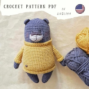 May include: Crochet pattern PDF in English for a blue and yellow crocheted bear wearing a yellow sweater. The pattern is available for download.